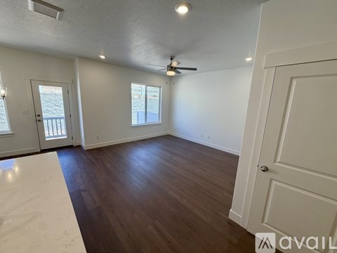 A room with wooden floors and white walls, featuring a ceiling fan and two windows.
