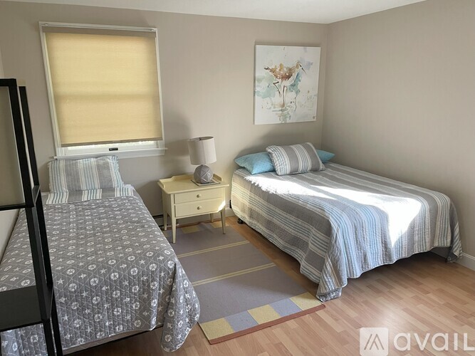 A bedroom with two beds, one with a grey patterned bedspread and the other with a blue striped bedspread.