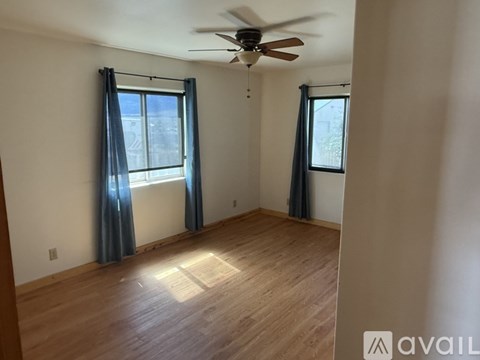 A room with a ceiling fan and two windows with curtains.