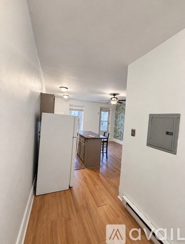 A white refrigerator in a narrow hallway with wood floors and white walls.