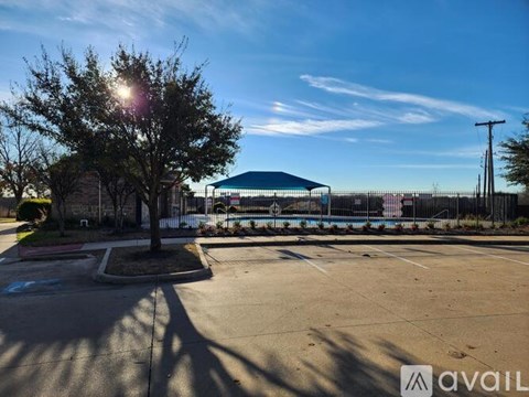 A sunny day in a parking lot with a tree and a pool in the background.