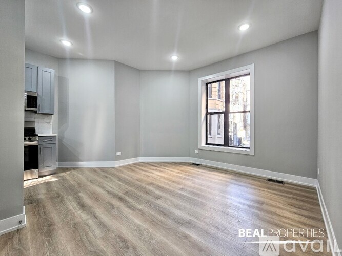A spacious room with wooden flooring and a window showing a cityscape outside.