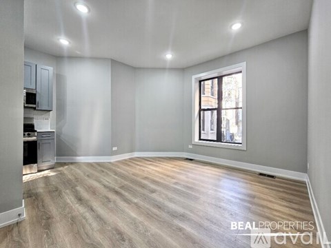 A spacious room with wooden flooring and a window showing a cityscape outside.
