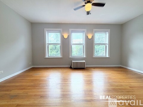 A spacious room with wooden floors and three windows.