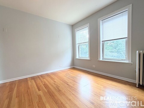 A room with wooden flooring and two windows.