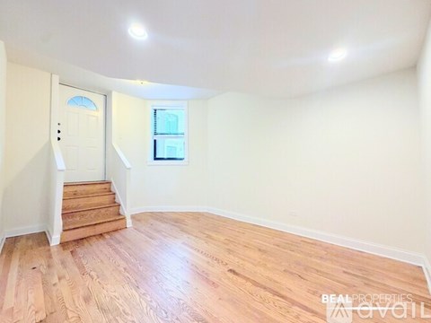 A room with wooden flooring and a staircase leading to another level.