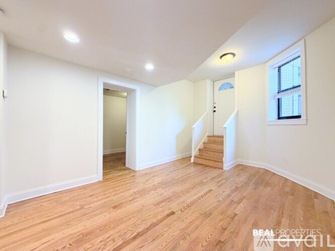 A spacious room with wooden flooring and a staircase leading to another room.