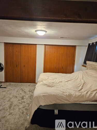 A bedroom with a bed, a fan, and two wooden doors.