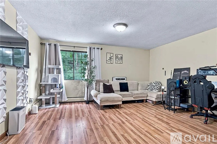 A living room with a couch, a chair, a desk with a computer, and a plant.
