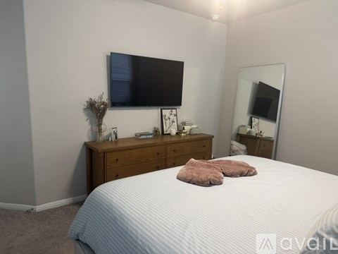A bedroom with a bed, a dresser with a mirror, and a TV mounted on the wall.