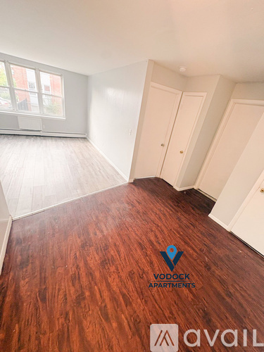 A room with wooden flooring and white walls, with a logo for Vodock Apartments on the floor.