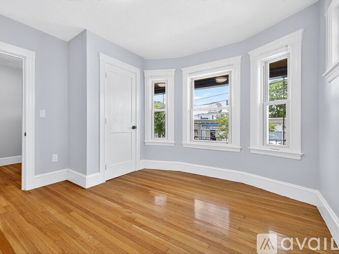 A room with wooden floors and white walls has a window with a view of a building outside.
