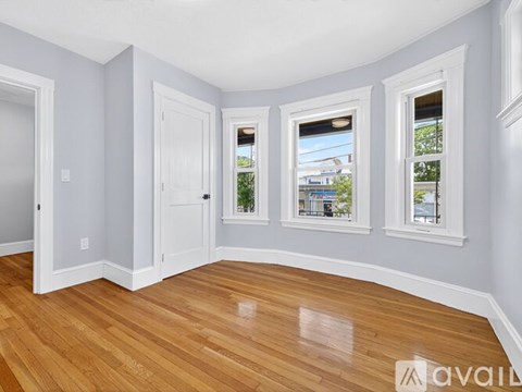 A room with wooden floors and white walls has a window with a view of a building outside.