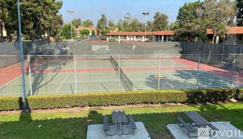 A tennis court surrounded by a fence and a green lawn.