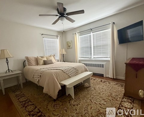 A bedroom with a bed, a bench, a fan, and a television.