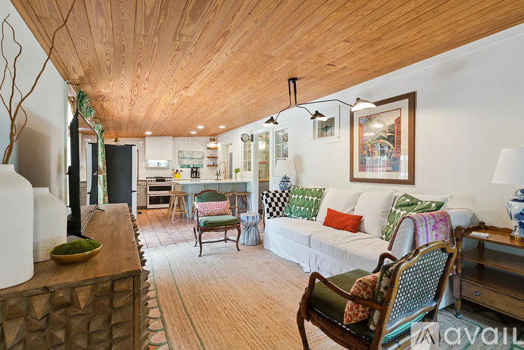 A living room with a wooden ceiling and a couch with green and white pillows.