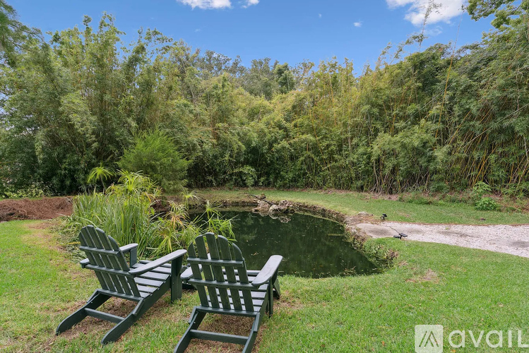 Two green chairs are placed on the grass near a pond.