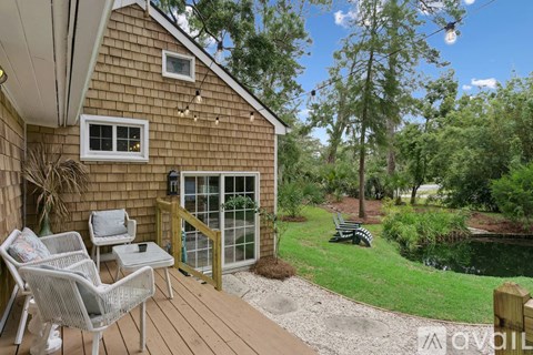 A wooden house with a deck and chairs overlooking a pond.