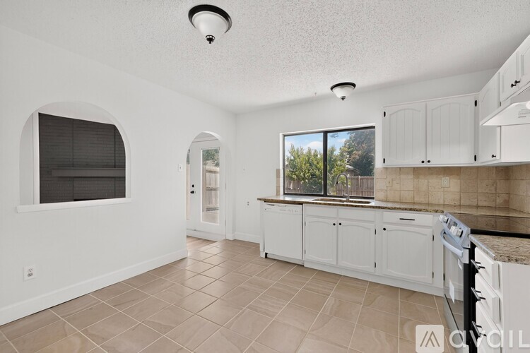 A kitchen with white cabinets and a window with blinds.