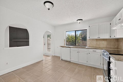 A kitchen with white cabinets and a window with blinds.