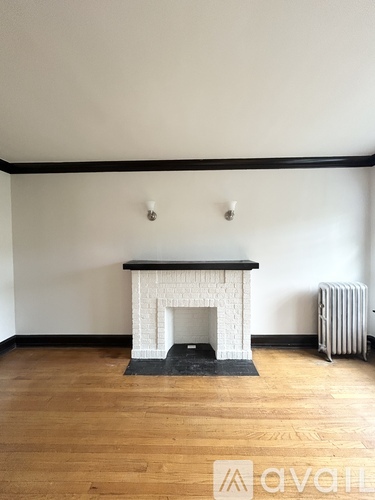 A white fireplace with a black mantle sits in a room with wooden floors.