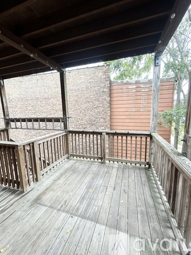 A wooden deck with a railing and a view of a brick wall and trees.