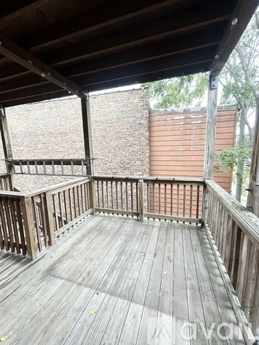 A wooden deck with a railing and a view of a brick wall and trees.