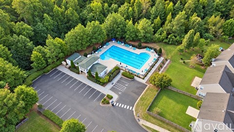 A pool surrounded by trees and a parking lot.