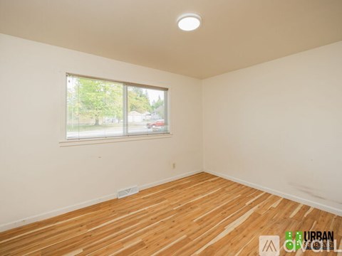 A room with wooden flooring and a window showing a view of trees and a car outside.