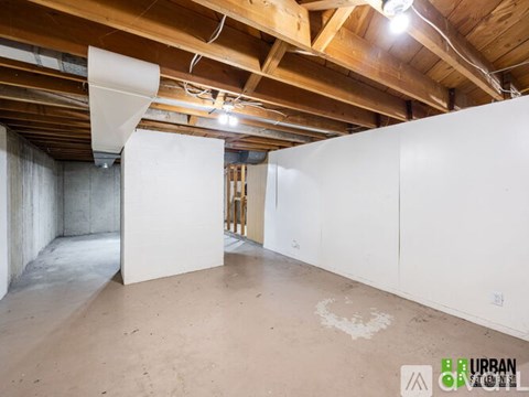 A spacious, unfinished room with wooden beams on the ceiling and a white wall on the left side.