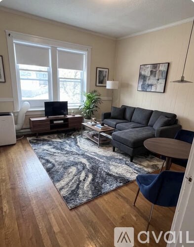 A living room with a grey couch, a black and white rug, and a wooden floor.