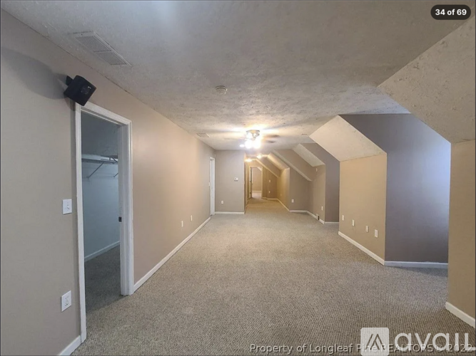 A spacious room with a door on the left and a hallway leading to another room on the right.