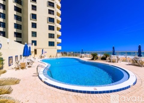 A large swimming pool is surrounded by lounge chairs and umbrellas.