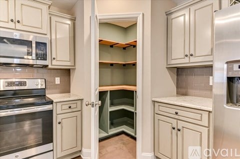 A kitchen with a stainless steel refrigerator and oven, and cabinets with a door open.