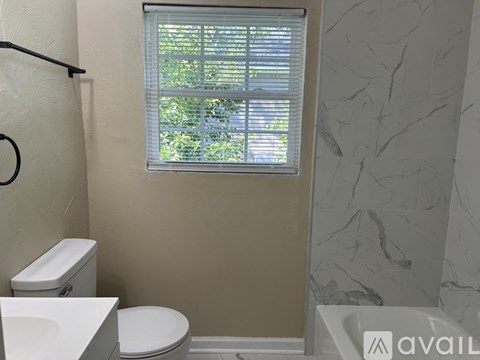 A bathroom with a toilet, a window with blinds, and a marble wall.