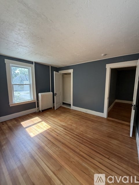 A room with wooden floors and a window with a view of a house outside.