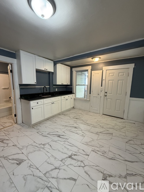 A kitchen with white cabinets and marble flooring.