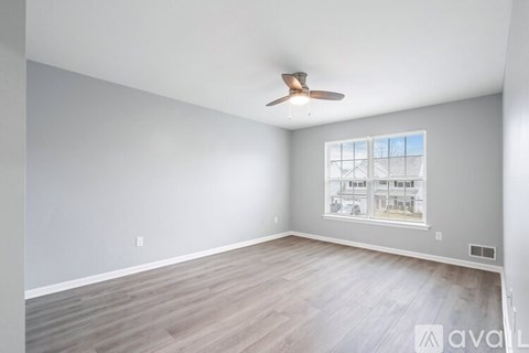 A room with a ceiling fan and a window showing a view of a building.