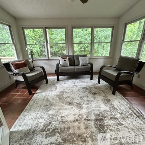 A living room with a rug and three chairs.
