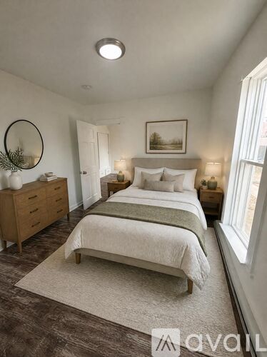 A bedroom with a bed, nightstand, and a round mirror on the wall.