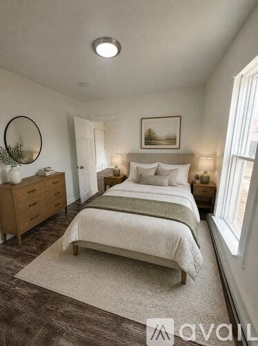 A bedroom with a bed, nightstand, and a round mirror on the wall.