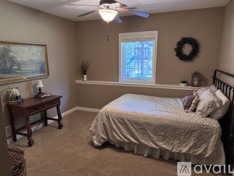A bedroom with a bed, a table, a window, and a wreath on the wall.