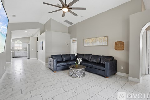 A living room with a black leather couch and a ceiling fan.