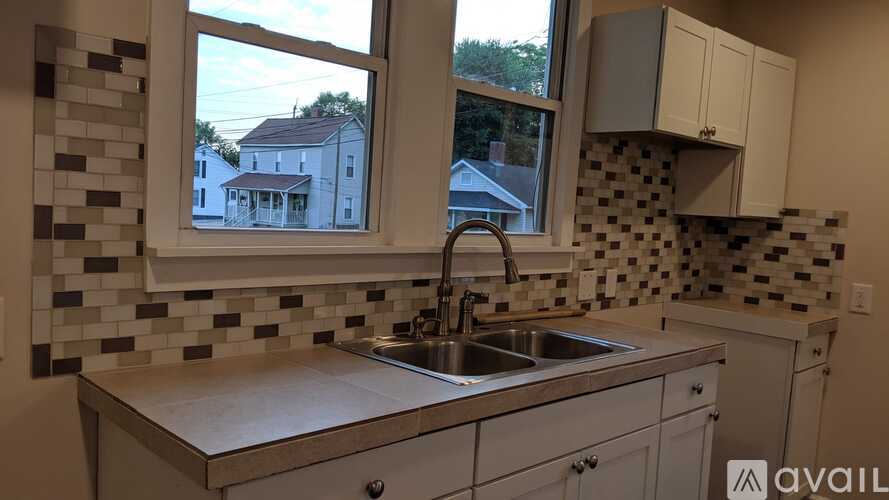 A kitchen with a sink and a window overlooking a house.