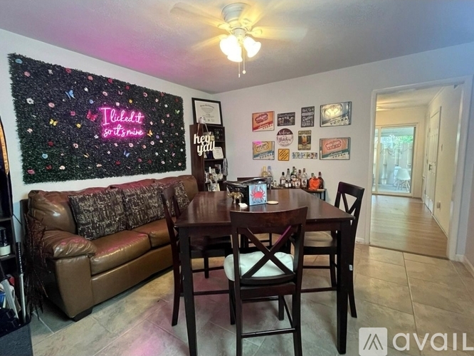 A room with a brown couch, a wooden table, and a wall with a neon sign that says "Tilidot".