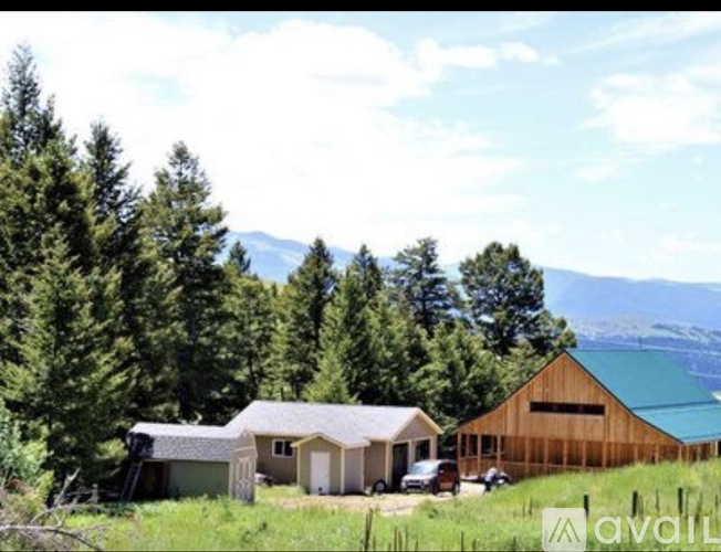 A wooden barn sits in a field with a mountain in the background.