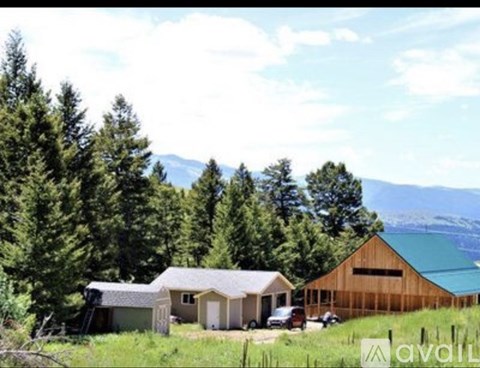 A wooden barn sits in a field with a mountain in the background.