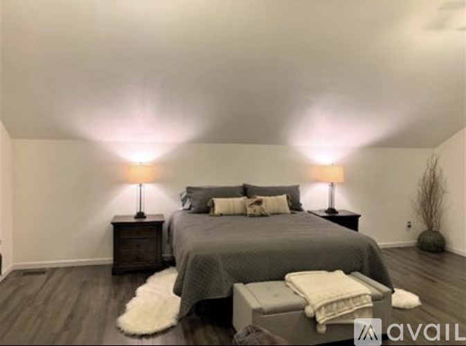 A bedroom with a bed, two lamps, and a white furry rug.
