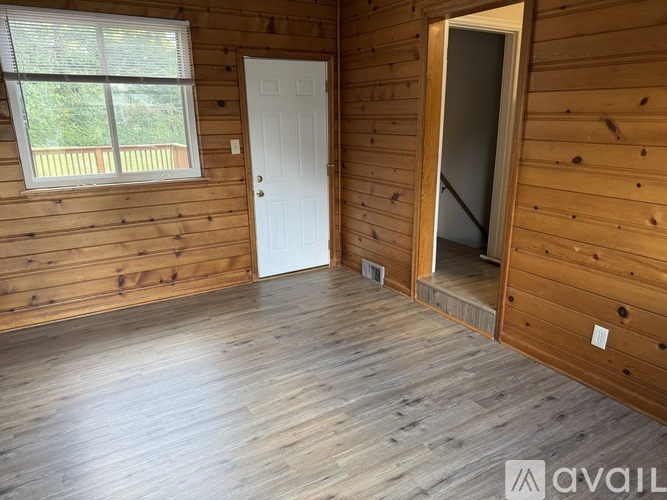 A room with wooden walls and floors, a white door, and a window with a view of a deck.