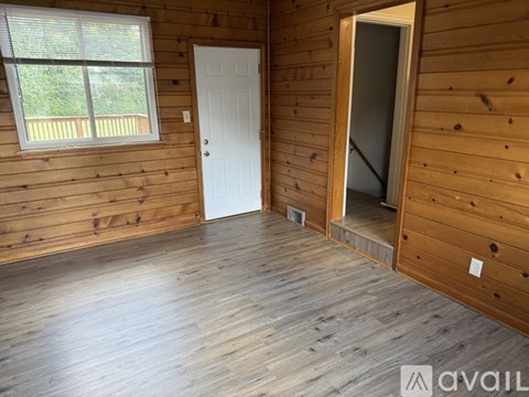 A room with wooden walls and floors, a white door, and a window with a view of a deck.